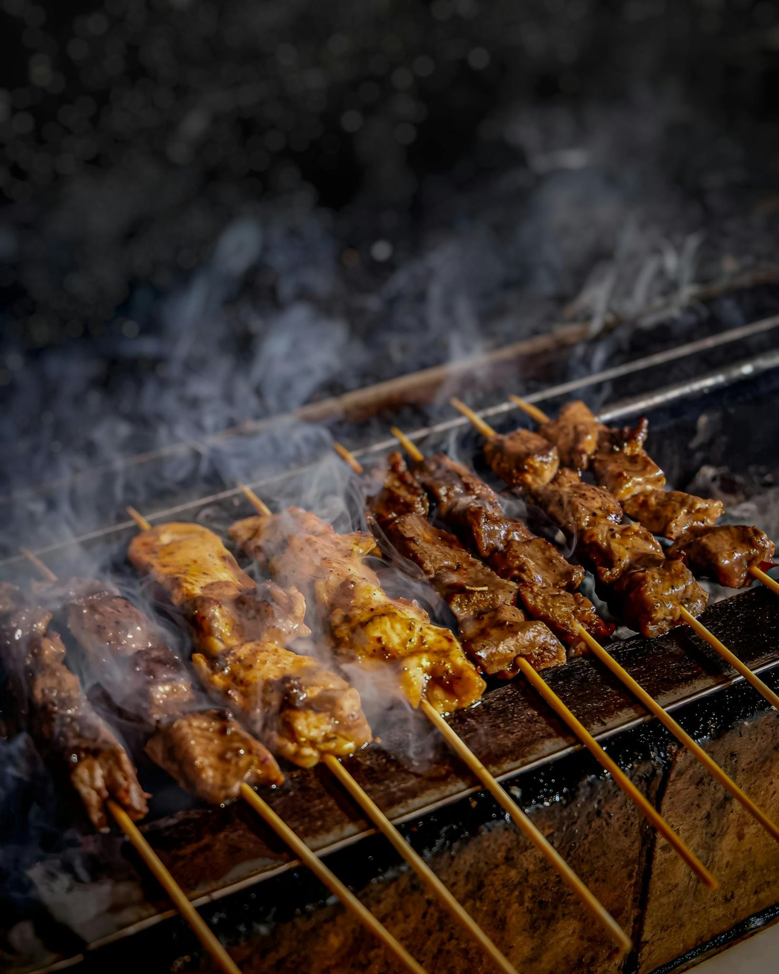 Delicious beef and chicken skewers grilling on a smoky charcoal barbecue in Subang, Indonesia.